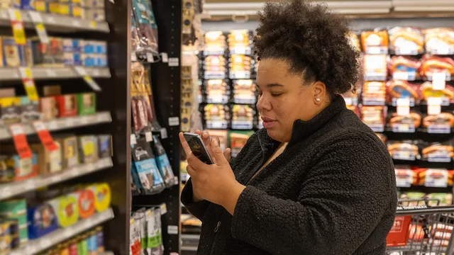 WIC shopper checks mobile phone application in a grocery store in Seattle, WA. (September 2024). Size-lookup vs staff-routed product request features